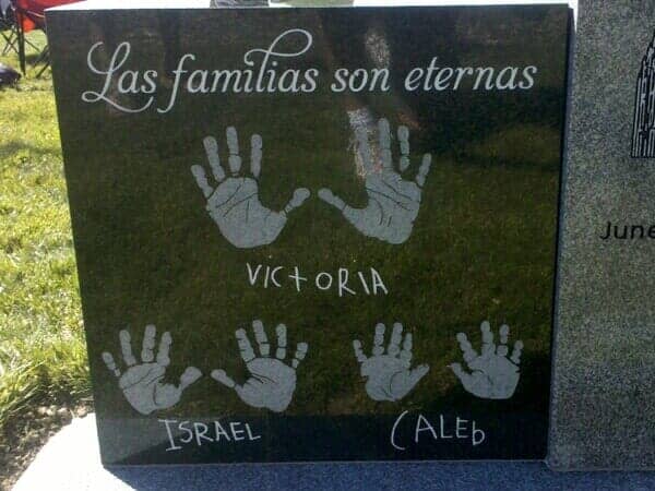 Children's handprints and Spanish lettering reading Las familias son eternas, sandblasted into black granite
