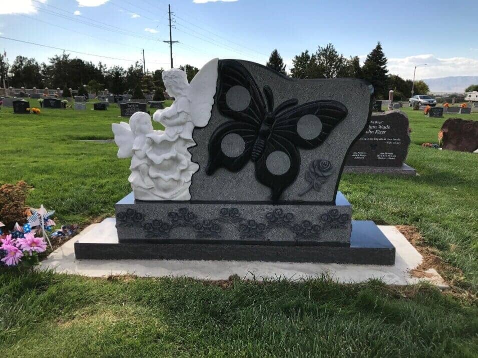 Granite monument with a carved butterfly and a white cherub sculpture