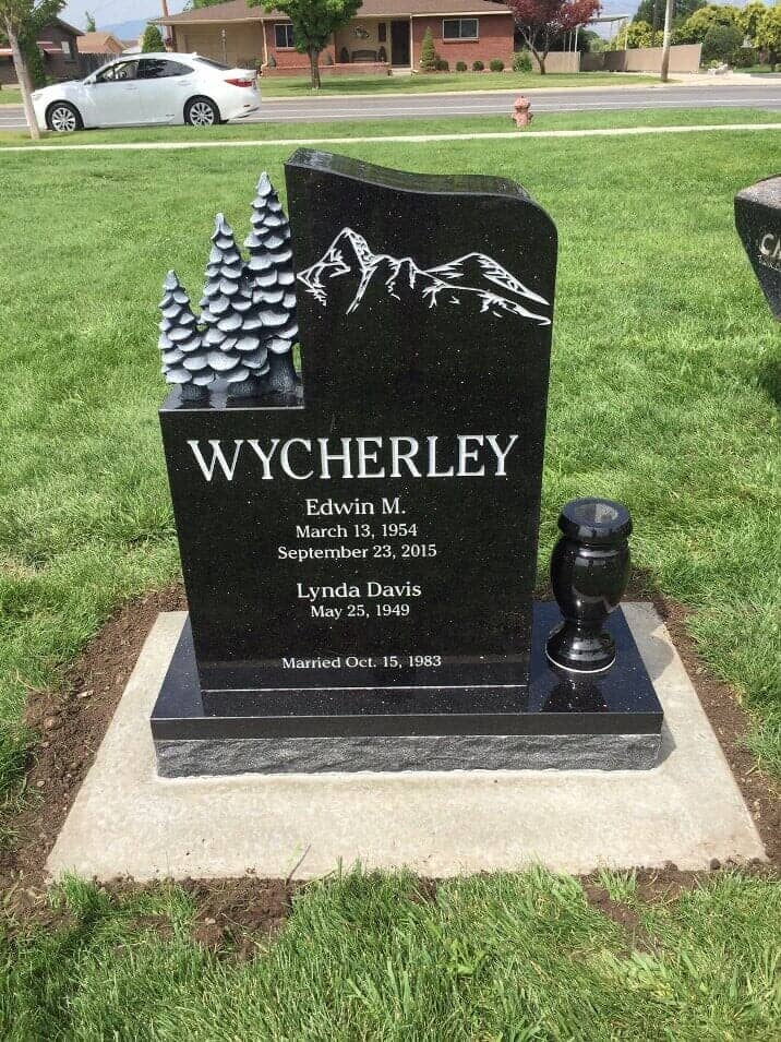 Black granite upright with carved pine trees and a mountain etching